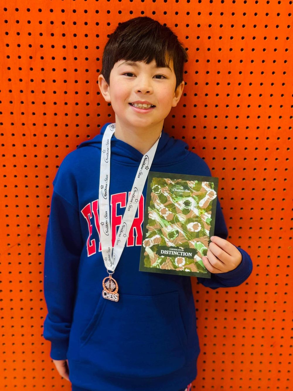 A student holding a chess medal and Distinction certificate