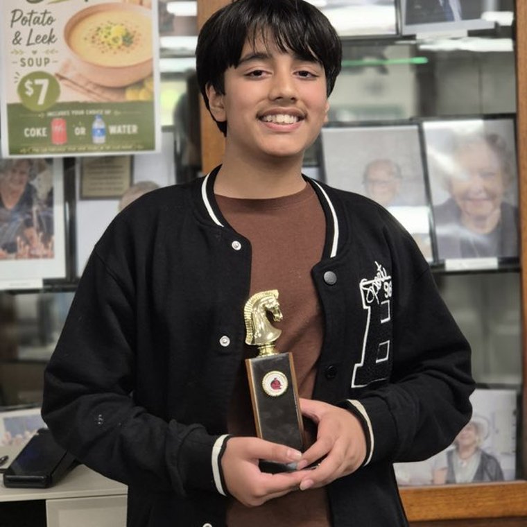 An Oz Chess Kids student holding a chess knight trophy